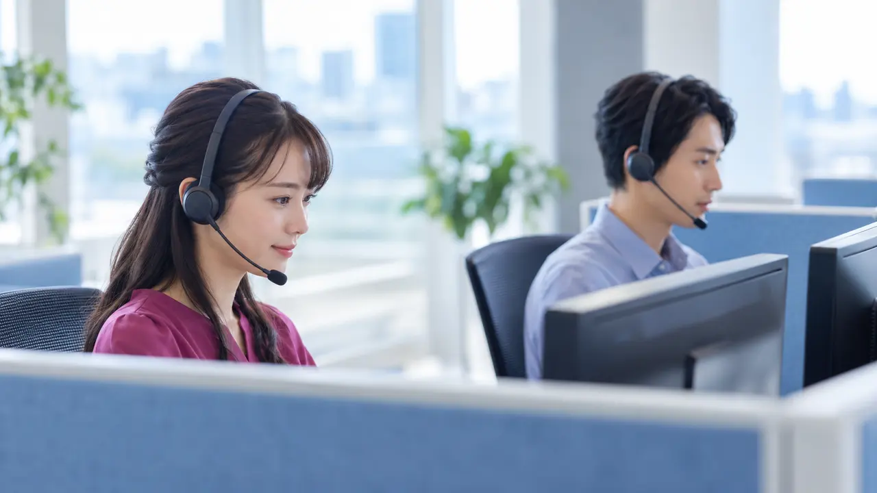 コールセンター 代行を検討する企業向けに、ヘッドセットを着用した二人の担当者がそれぞれの画面で問い合わせ対応を行う明るい現場