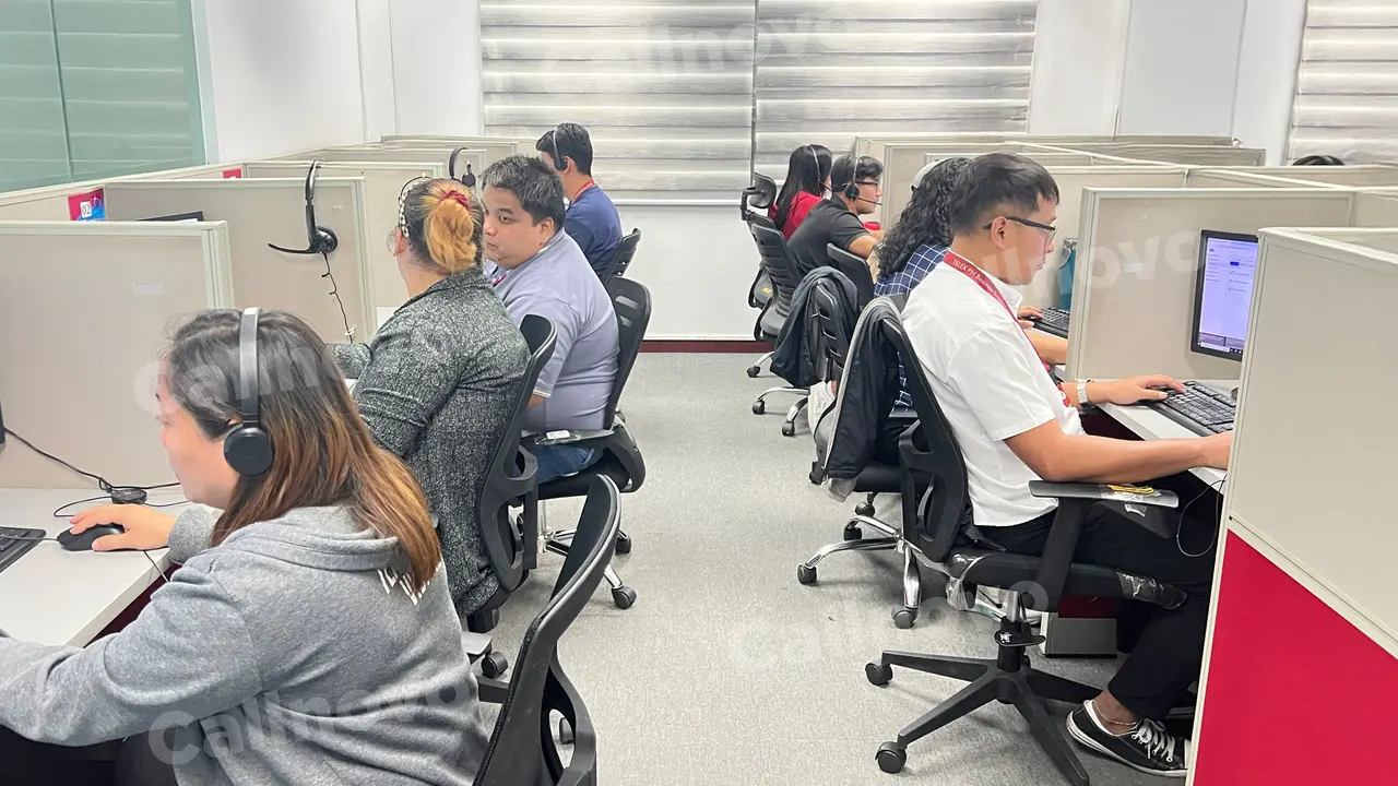 Agents wearing headsets handle customer contacts at a row of desks on a busy contact center floor — customer inquiry volume