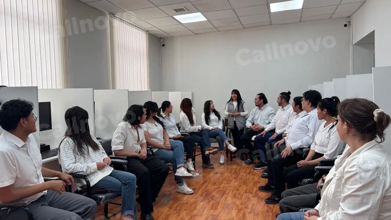 A team of support staff sits in a circle in a training room while one colleague stands and speaks to the group — customer service quality assurance