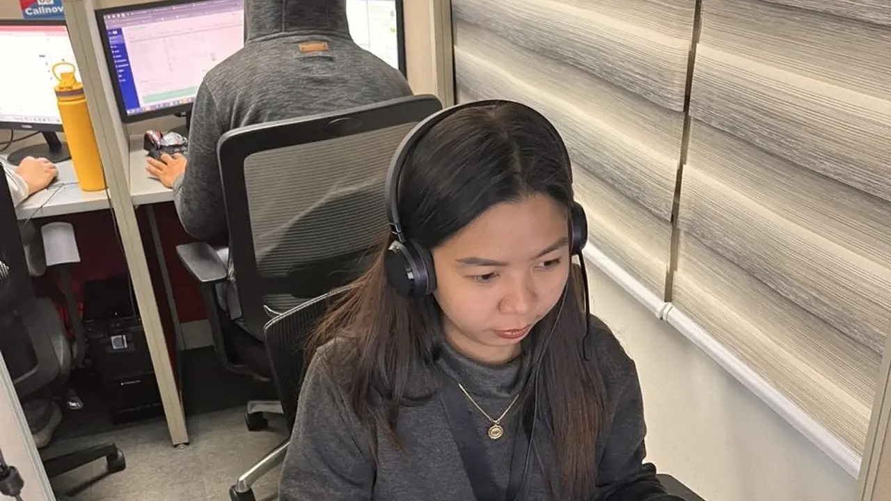 A support agent wearing a headset looks at her screen at a desk beside a window with blinds — healthcare call center outsourcing