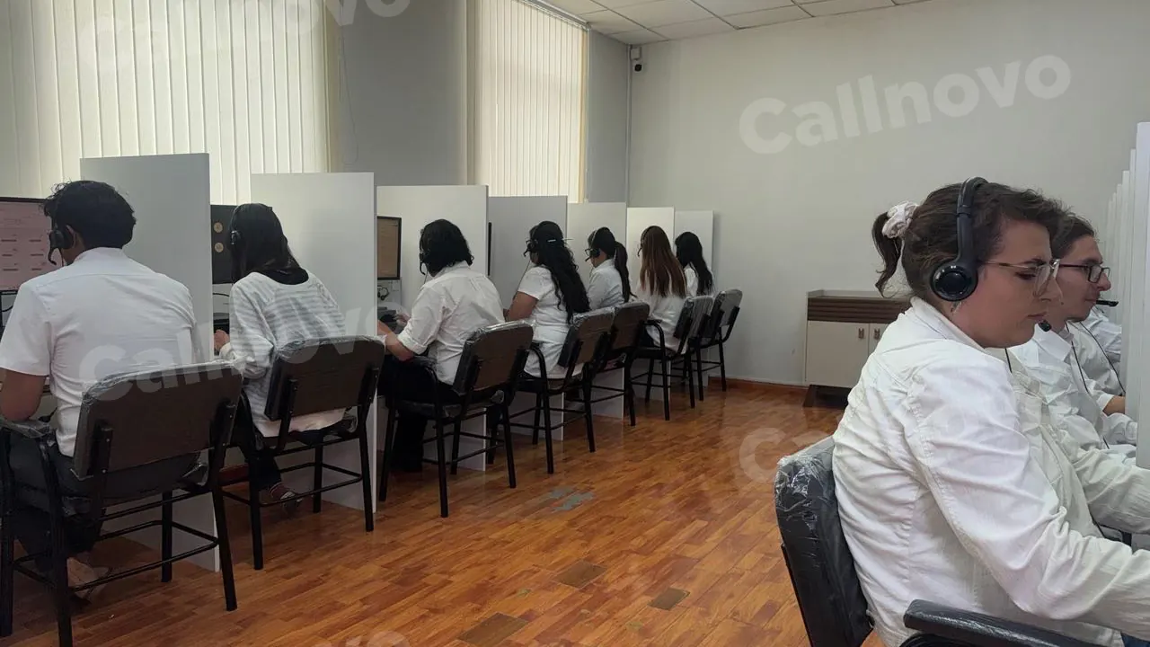 Agentes en formación con auriculares practican en una fila de escritorios en una sala de capacitación de Callnovo