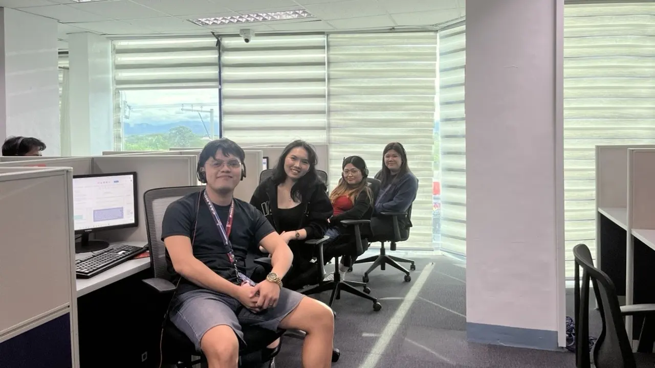 Four members of a support team sit together beside a workstation near the windows of a contact center floor — multilingual call center services
