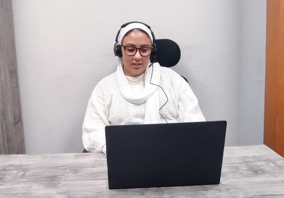 A Callnovo.ai human agent wearing a headset talks with a caller while working on a laptop at a plain desk