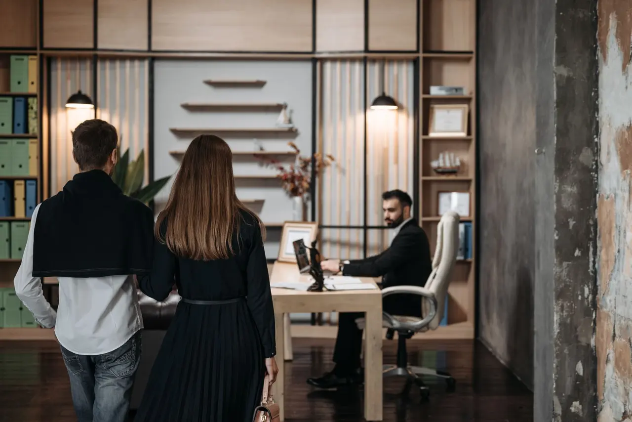 A couple walking into a law office toward the attorney at his desk — a new-matter intake beginning