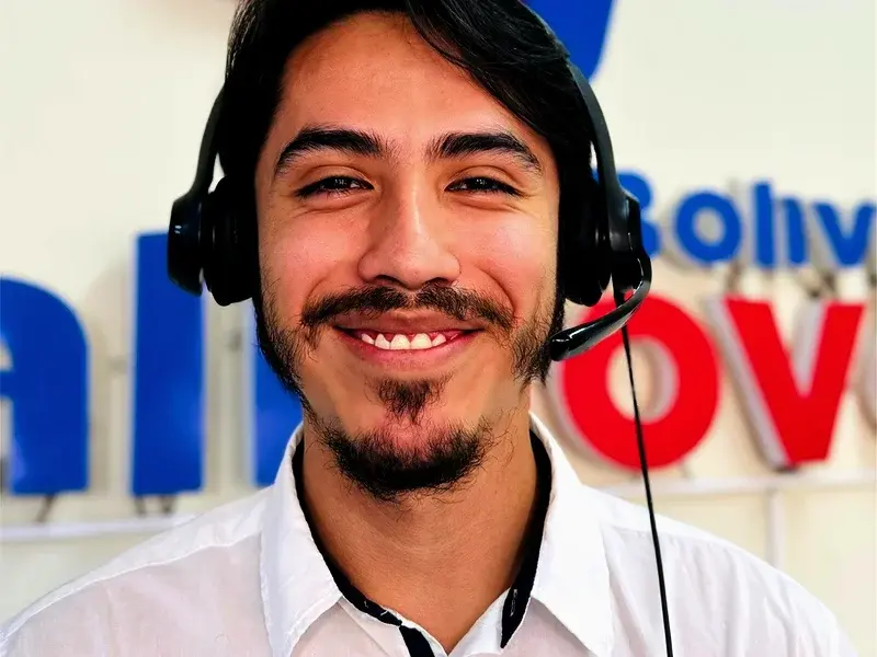 A Callnovo support agent wearing a headset smiles in front of the Callnovo Bolivia sign