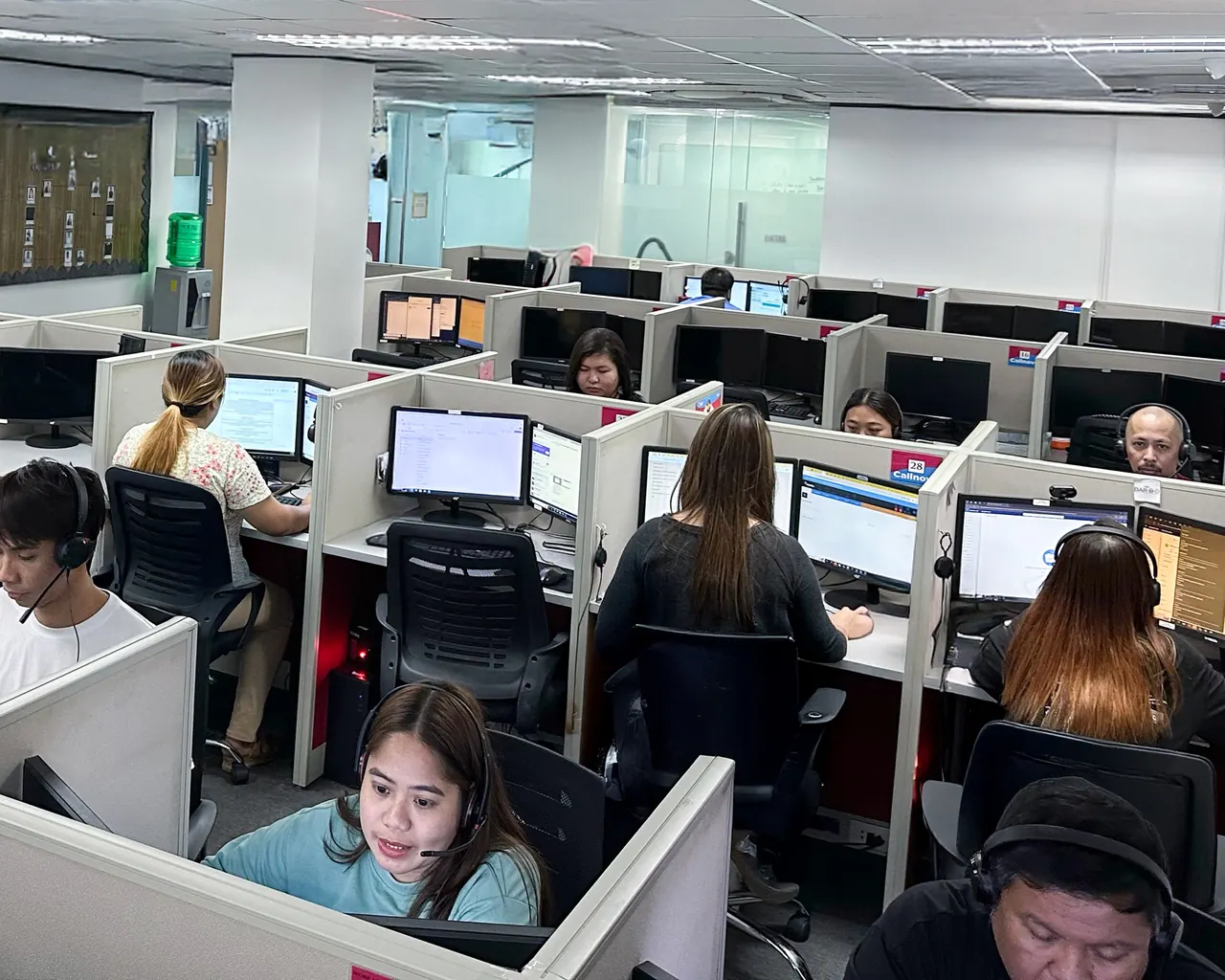 Support agents wearing headsets work at partitioned desks on a busy Callnovo contact center floor